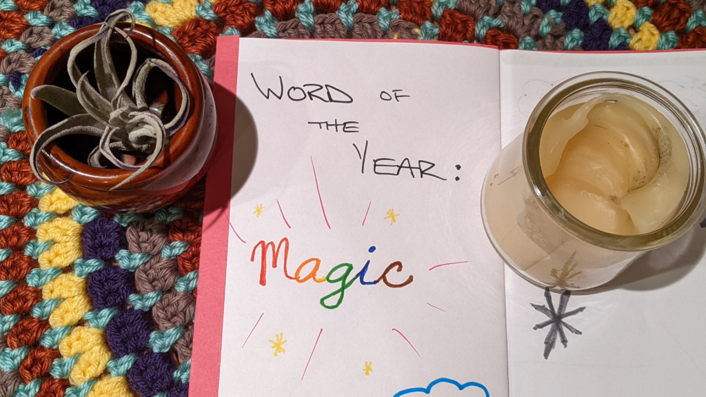 open book with the words "Word of the Year: Magic" along side a candle and air plant